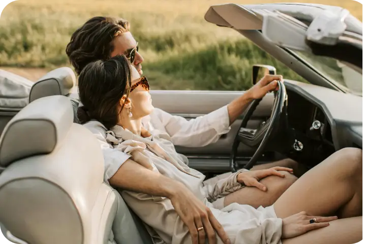 Een stijlvol stel dat in een open luxe auto door een schilderachtige plattelandsomgeving rijdt.