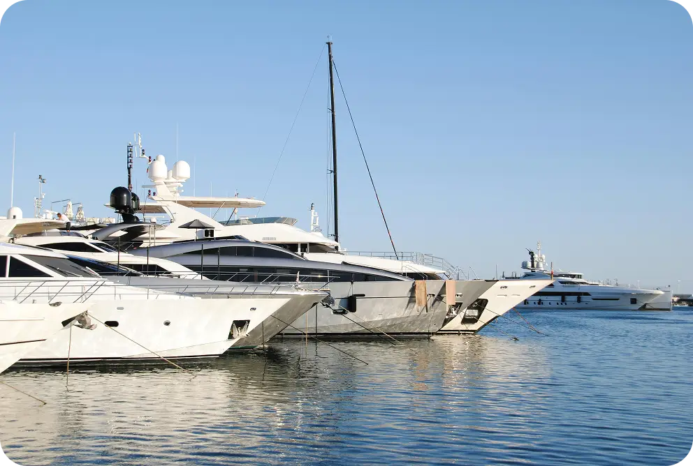 Verschillende luxe jachten aangemeerd in een marina met kalm water en een heldere blauwe lucht die een elegante sfeer creëren.
